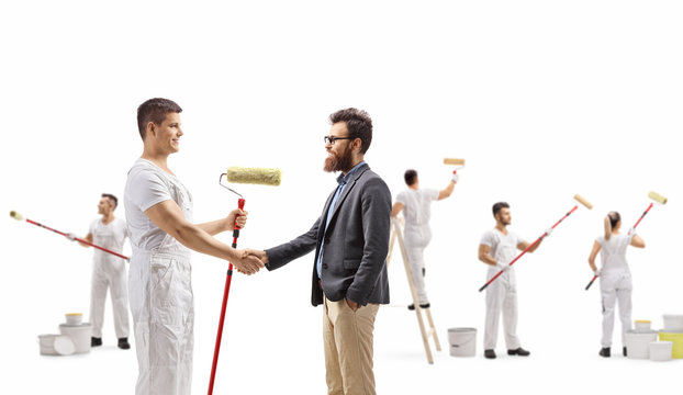 Male wall painter shaking hands with a man and people painting wall behind