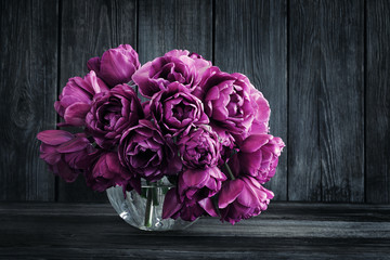 Bouquet of purple tulips in a vase on a wooden wall background