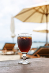 Cola glass on beach with umbrellas. Cooling drink