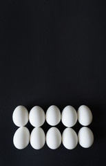white chicken eggs lie exactly in line, ordered on a black isolated background, top view