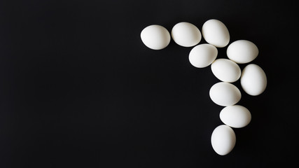 white chicken eggs lie chaotically on a black isolated background, corner composition, top view