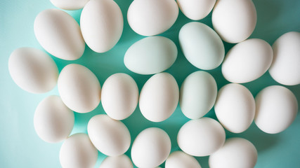 Organic white chicken eggs with pale blue accents chaotically lie on a blue background texture top view