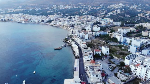 Quiet small town at North shore of Crete Island, aerial shot at early morning time. Camera slowly soar over strand street, dense build with low rise buildings, restaurants and hotels area