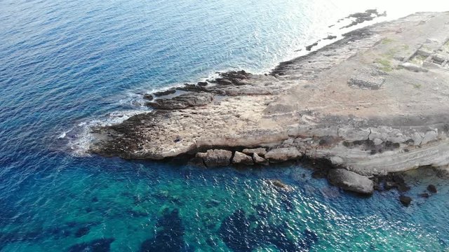 Flat stony shelf washed by crystal sea waters, aerial shot at sunny morning time. Old ruins seen at right. North coast of Crete island