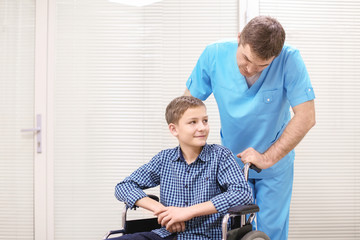 Male doctor taking care of little boy in wheelchair indoors
