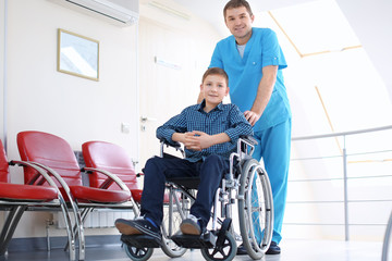 Male doctor taking care of little boy in wheelchair indoors