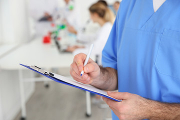 Medical student with clipboard working in scientific laboratory, closeup. Space for text