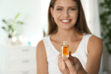 Young woman holding eyelash oil indoors, closeup