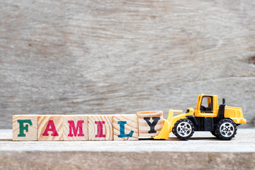 Toy bulldozer hold letter block y to complete word family on wood background