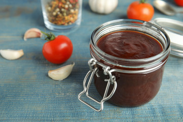 Jar with tasty barbecue sauce on blue wooden table. Space for text