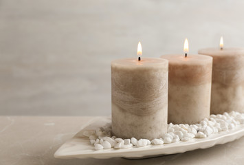 White plate with three burning candles and rocks on table. Space for text