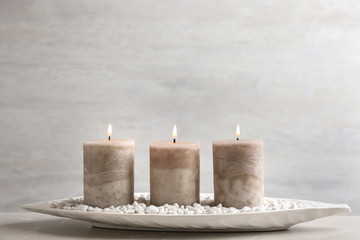Fototapeta na wymiar White plate with three burning candles and rocks on table