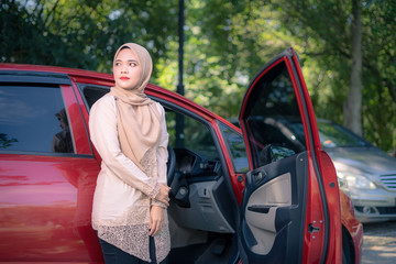 Young Muslim standing besides car, female driver concept.