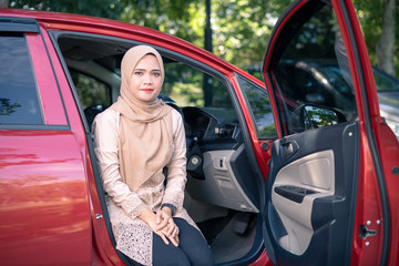 portrait of young muslim woman in hijab sitting on car seat with opened door. Female driver concept.