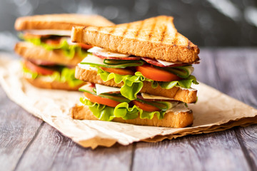 Sandwich with cheese, tomato, cucumber, sausage and salad on wooden background. Horizontal...