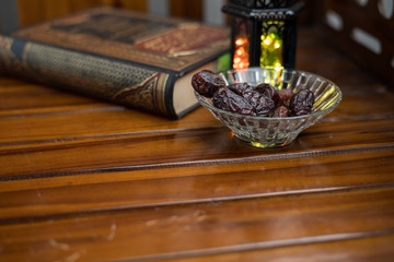 Islamic, ramadan and praying concept. Arabic lantern, dates or kurma with arabic book known as kitab or Quran on classic shine wood background, copy space, selective focus.