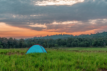 landscape scenery of camping tent on grass field with background of forest and mountains and sunrising sky in natural park
