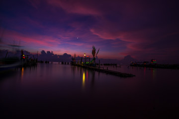 Fototapeta premium The blurred background of the morning twilight by the sea, changing the color of the beautiful sky, there is a fishing boat docked waiting to go out to find fish again.
