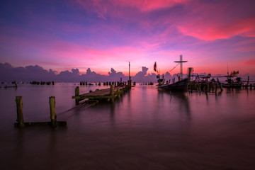 Obraz premium The blurred background of the morning twilight by the sea, changing the color of the beautiful sky, there is a fishing boat docked waiting to go out to find fish again.