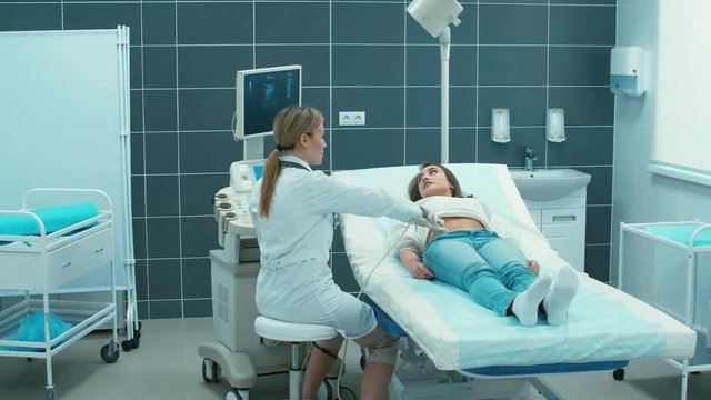 Young woman having abdomen ultrasound examination in clinic with female doctor