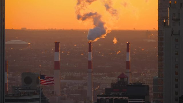 Close up American flag waves beneath the industrial chimney emitting smoke harmful smoke from a power plant on the outskirts of new York