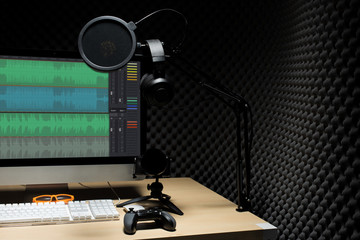 Microphone Condenser, gold mic hang over sound absorbing wall room with wave monitor keyboard mouse game pad controller and headphone in dark audio studio, low exposure lighting background copy space