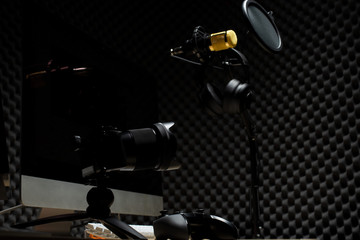 Microphone Condenser, gold mic hang over sound absorbing wall room with wave monitor keyboard mouse game pad controller and headphone in dark audio studio, low exposure lighting background copy space