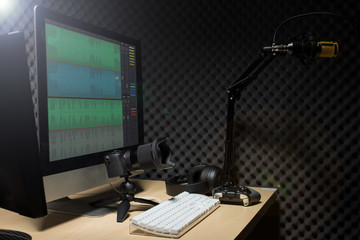 Microphone Condenser, gold mic hang over sound absorbing wall room with wave monitor keyboard mouse game pad controller and headphone in dark audio studio, low exposure lighting background copy space