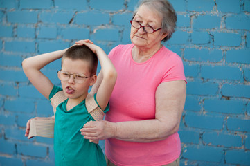 elderly woman in pink T-shirt and glasses wears corset to correct posture for her grandson. child...