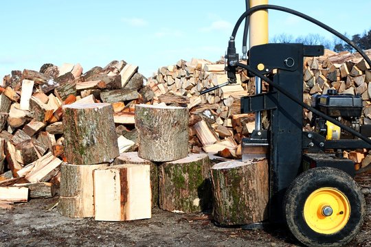 Yellow and black log splitter on end to split vertically with blocks, heap and woodpile 