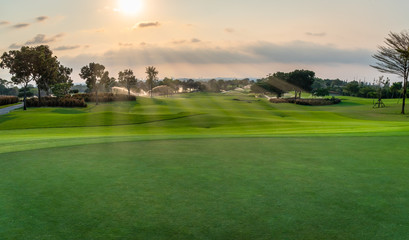 The beautiful green view of green grass and sand banker on golf course with sun cloudy sky background.