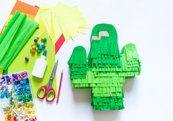 Fototapeta premium Diy cinco de mayo Mexican Pinata cactus made cardboard and crepe paper your own hands on a white background.