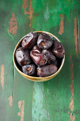 Large Medjool Dates in a bowl. Closeup view on green wooden rustic background