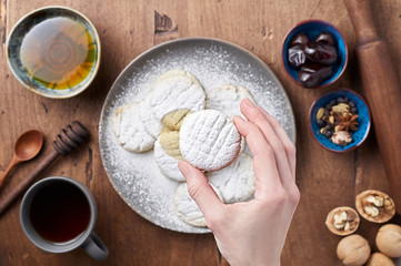 Hand holds Arabic homemade cookies filled with dates and walnuts covered powdered sugar