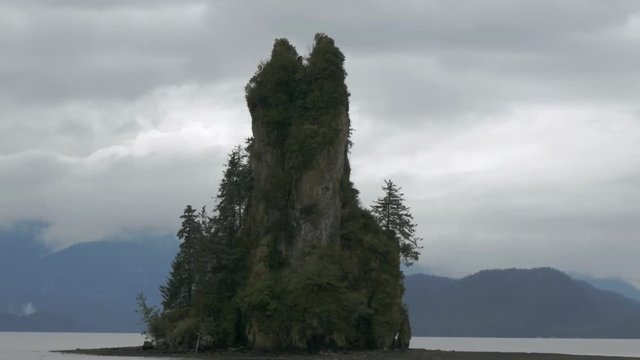New Eddystone Rock sits on an isle in Alaska. Mountains and ocean are visible in the background as the camera passes.
