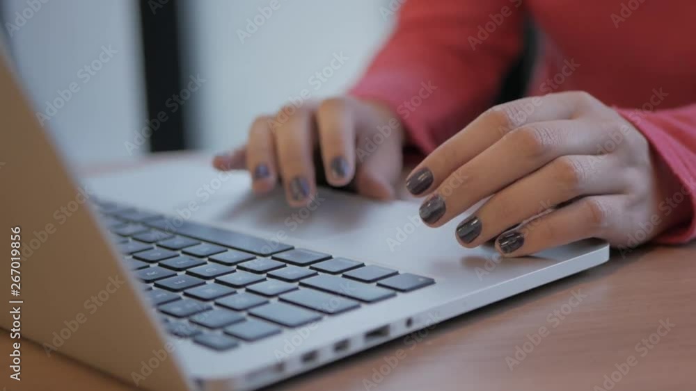 Poster female hands typing on a notebook on a table top. she is in a red blouse, and her nails are painted 