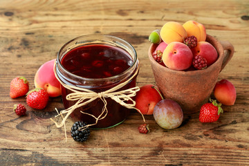 Jar of strawberry jam among summer and autumn fruits