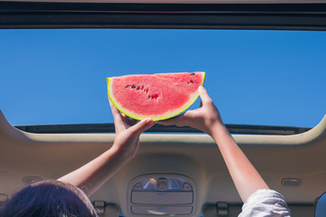 Two girls traveling by car and holding slice of watermelon in open hatch of a vehicle. Travel...