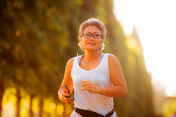 middle aged 40s or 50s happy and attractive woman with grey hair training at city park with green...