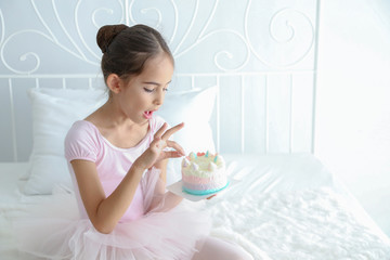 Cute little child girl in pink dress was picking birthday cake to eat on the bed. 