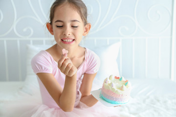 Cute little child girl in pink dress was holding pink heart chocolate from birthday cake to eat on the bedroom background. 