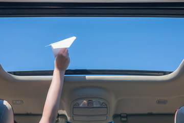 A girl is launching a paper airplane from open hatch of the car during summer vacation. Travel and...