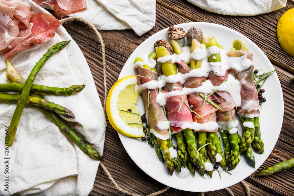 Wall mural fresh cooked green asparagus with ham and sauce on plate, top view