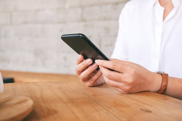 Closeup image of a woman holding , using and looking at smart phone on wooden table