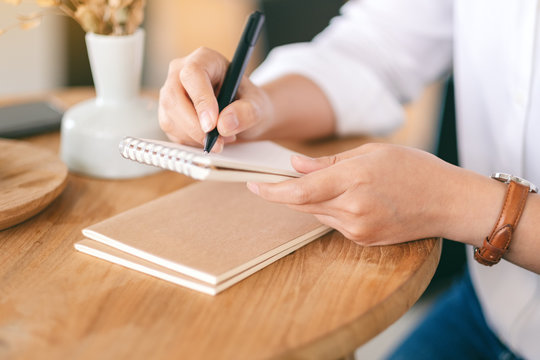 Closeup image of a woman holding and writing on a blank notebook on wooden table