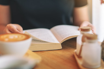 Closeup image of a woman holding and reading a vintage novel book on wooden table