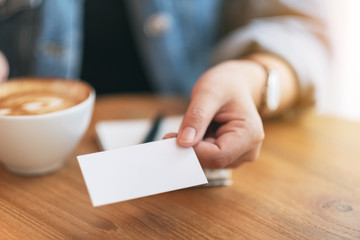 A woman holding and giving a blank empty business card to someone while drinking coffeeA woman holding and giving a blank empty business card to someone while drinking coffee