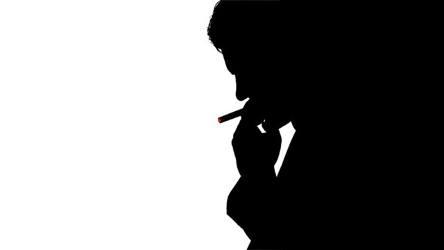 Silhouette of smoking man with burning cigarette.Silhouette of a man smoking a cigarette. He takes a drag, then lets out a puff of smoke that slowly dissipates. He is contemplating his life choices an