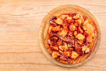 Pulpo a la gallega, octopus with potatoes and paprika, a typical Spanish Galician dish, on a traditional wooden plate, shot from the top on a wooden background with a place for text