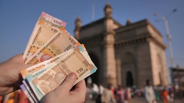 A man considers Indian rupees against the background of the Gate of India in the city of Mumbai. Hands close up.